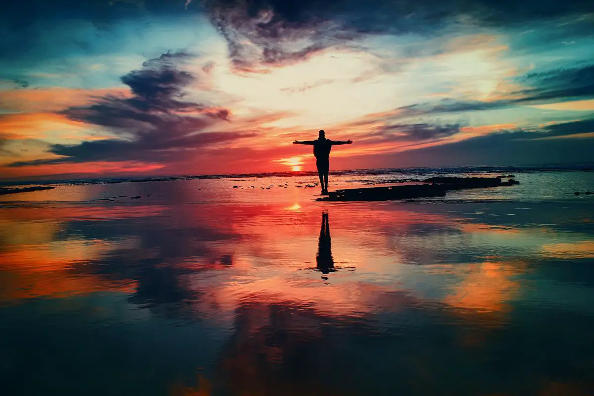 A person standing on a cliff, looking towards the horizon with their arms stretched out, as if they are flying. This image describes the feeling of freedom and empowerment someone might experience during a dream of flying without wings.