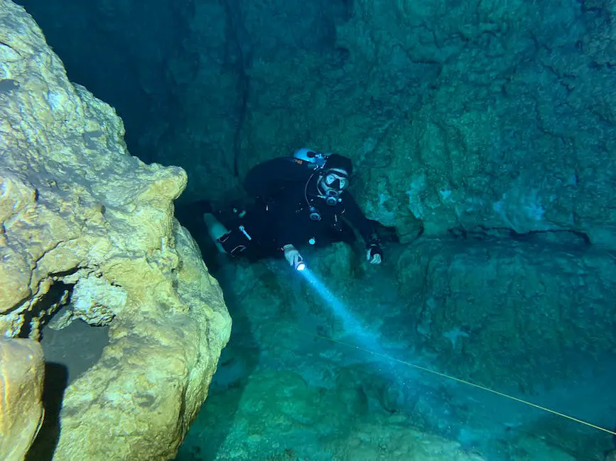 A diver in an underwater cave exploring the limestone formations with a flashlight.
